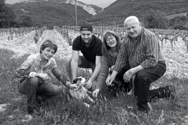 Photo en noir et blanc de quatre personnes accroupies dans une vigne, avec un chien au centre