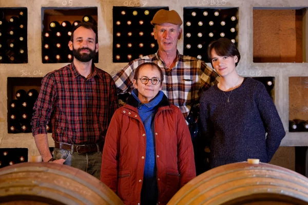 Une photo de famille prise dans la cave du domaine. Les membres de la famille se tiennent fièrement devant des rangées de bouteilles de vin
