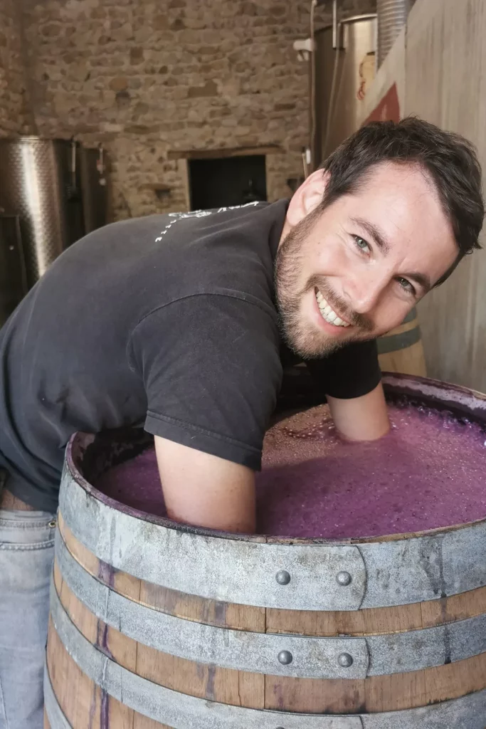 Julien Bertrand, souriant, avec les bras plongés dans une barrique de fermentation