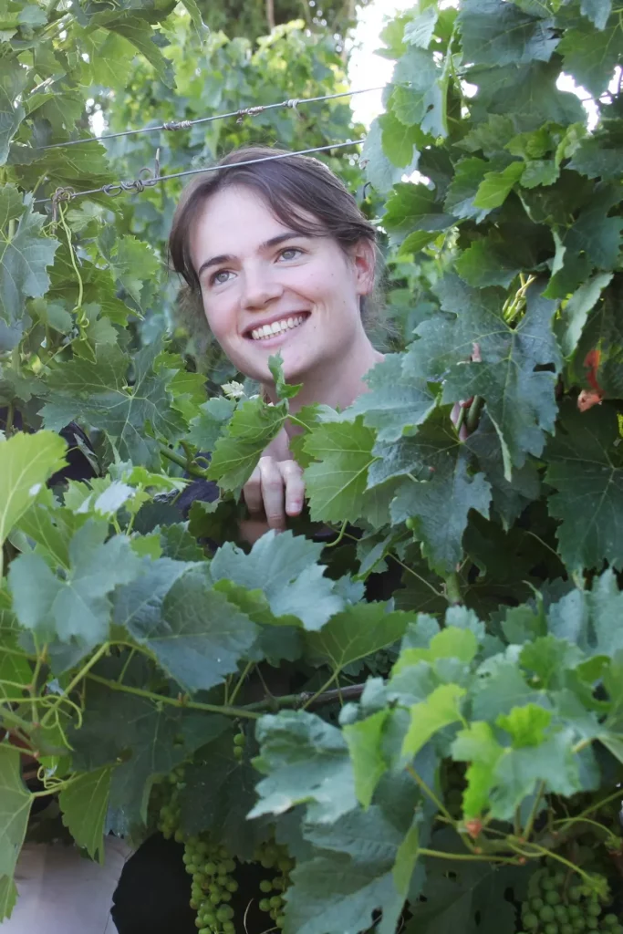 Marion, souriante, se tient parmi les feuilles vertes des vignes