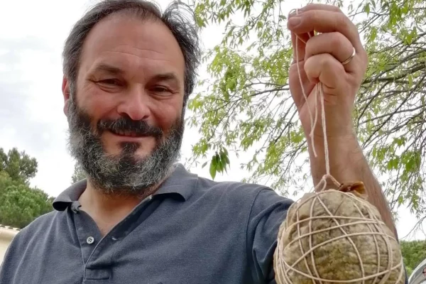 Vigneron barbu tenant une boule de ficelle à la main, souriant devant un arbre.