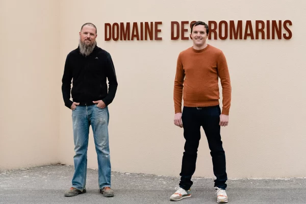 Deux vignerons posant devant un mur avec l'inscription "Domaine des Romarins"