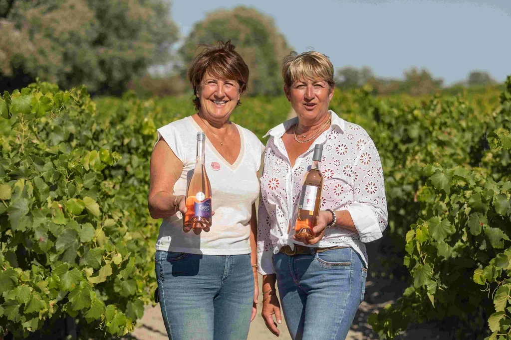 Brigitte et Nathalie souriantes dans le vignoble, tenant des bouteilles de vin rosé