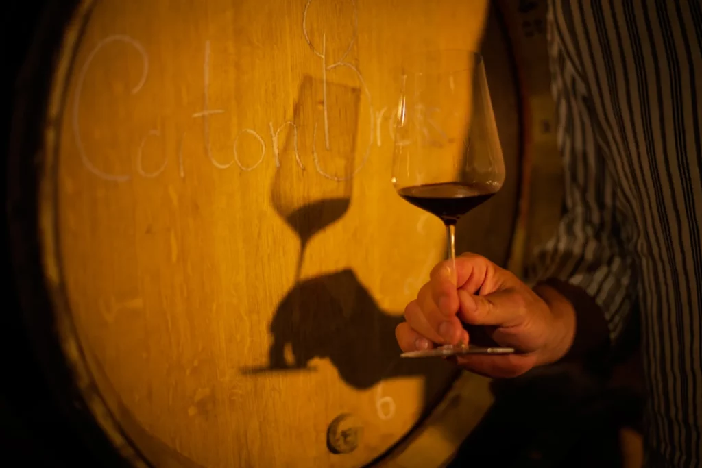 Domaine Chandon de Briailles - Verre de vin rouge levé devant un fût écrit à la craie