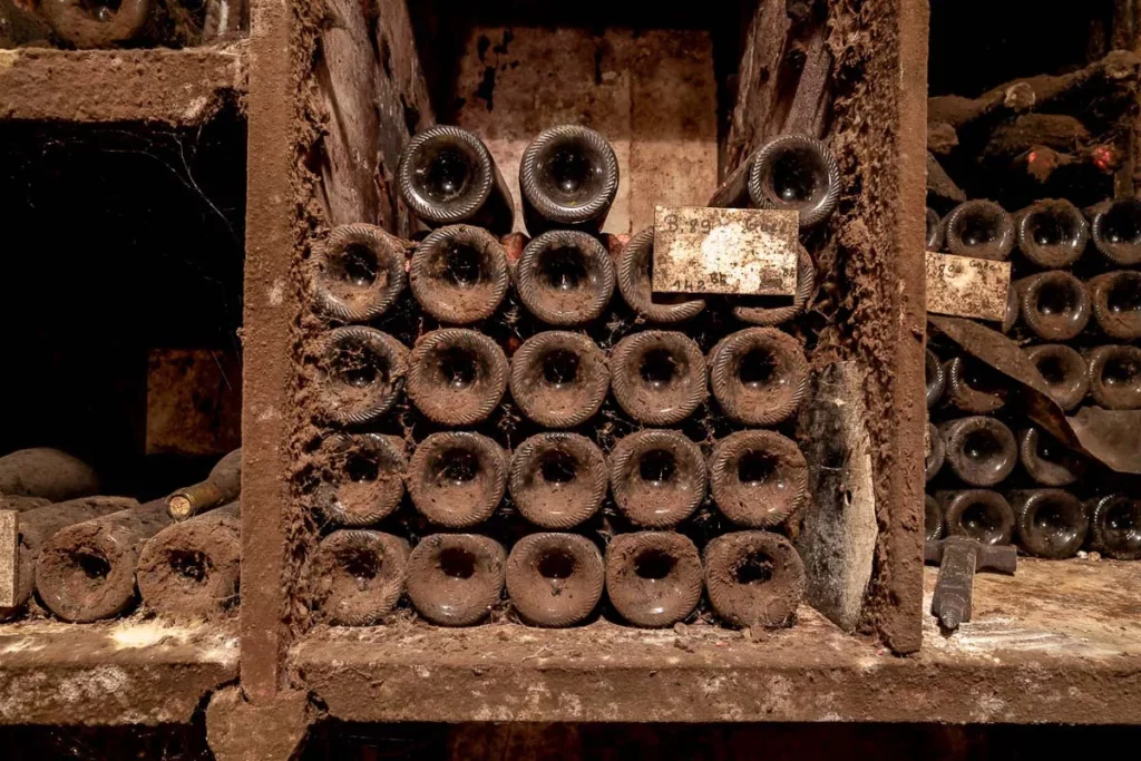 Domaine Henri Delagrange - Vieux flacons couverts de poussière dans les casiers de la cave