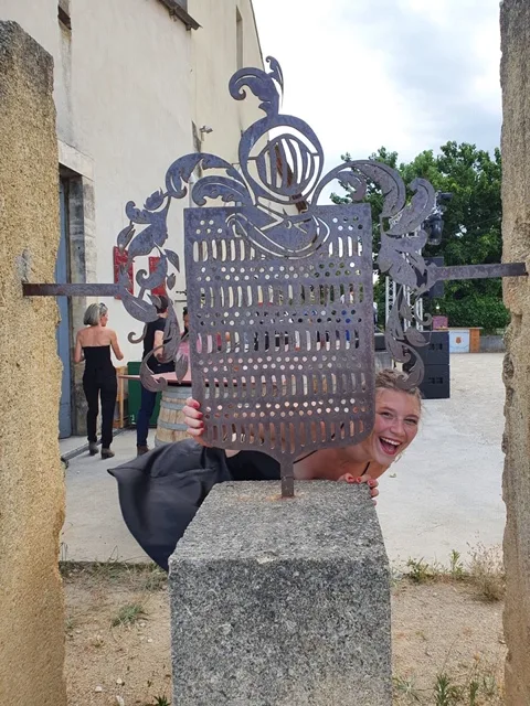 Château d'Or et de Gueules - Une jeune femme rieuse derrière un blason en fer forgé