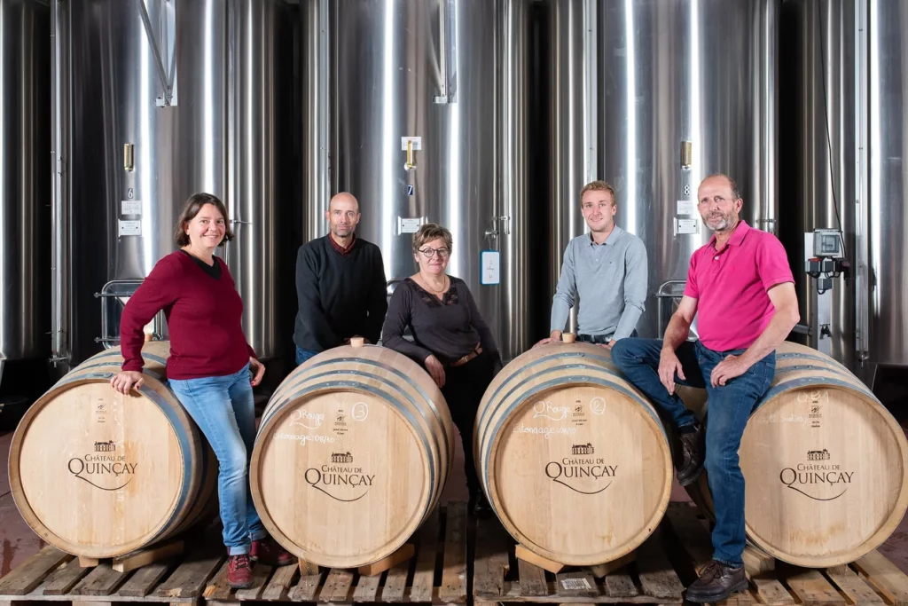 Château de Quinçay - Cinq personnes du domaine assises sur des barriques, devant les cuves inox