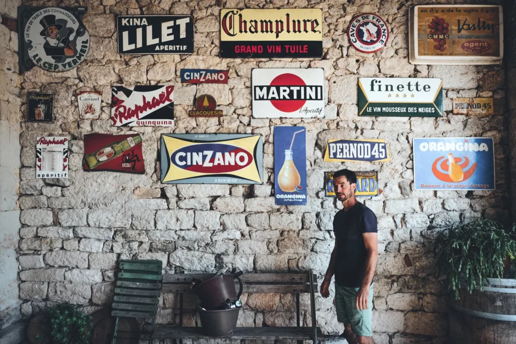 Domaine de Brin - Damien Bonnet devant un mur de pierre couvert de vieilles plaques émaillées