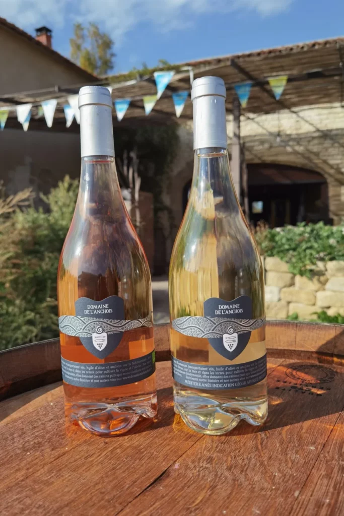 Domaine de l’Anchois - Un rosé et un blanc du domaine posés sur un tonneau, dans une cour fleurie