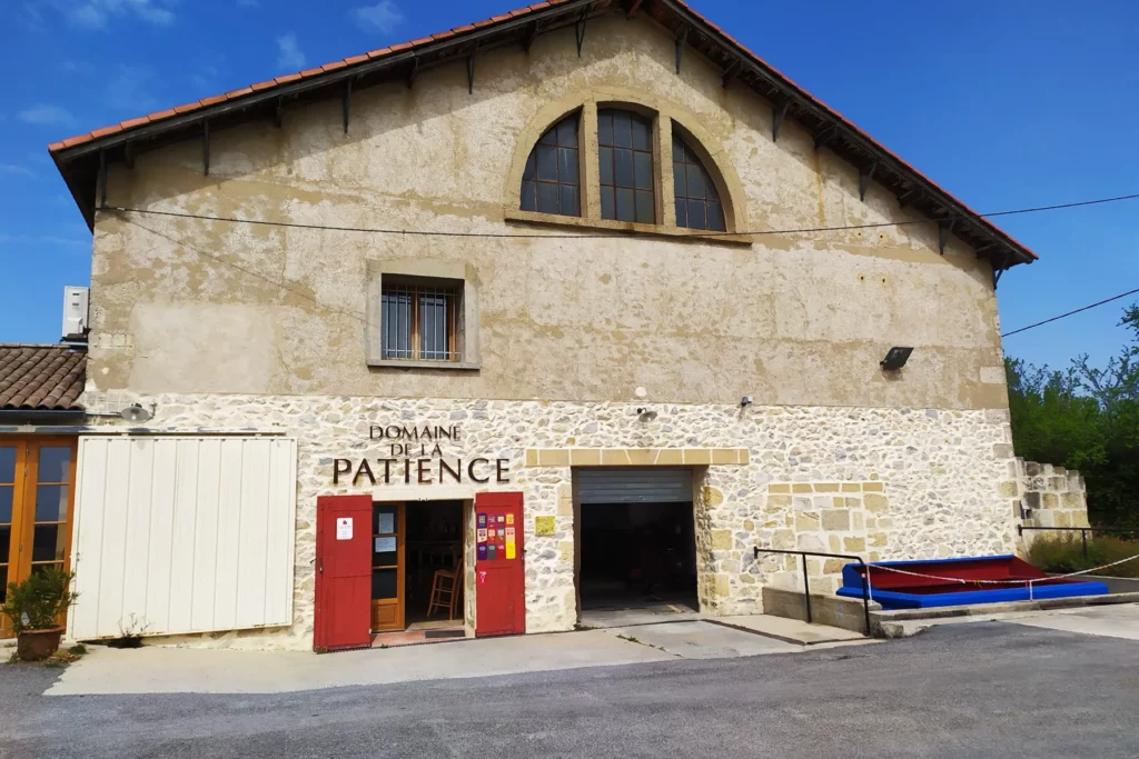Domaine de la Patience - Façade en pierre de taille de la cave, le nom du domaine au-dessus des portes rouges à Bezouce