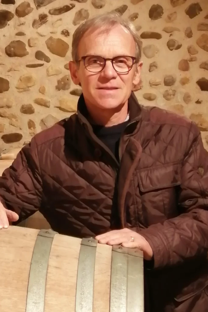Domaine Nigri - Jean-Louis Lacoste accoudé à une barrique devant un mur de galets