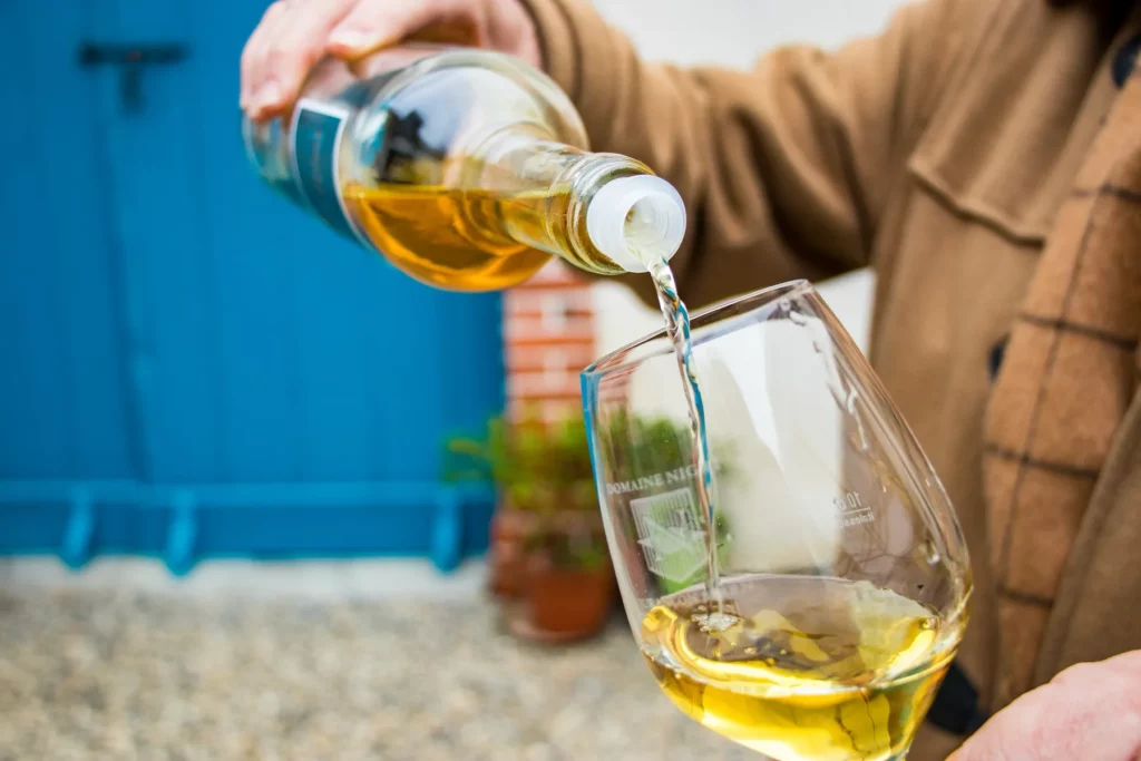 Domaine Nigri - Un jurançon doré versé dans un verre devant une porte bleue