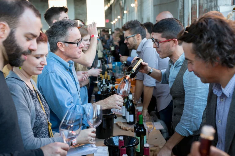 RAW WINE - Un vigneron sert un vin rosé à des visiteurs qui se pressent autour de sa table de dégustation