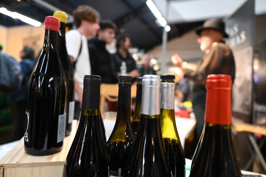 Salon Marjolaine - Bouteilles de vin sur le comptoir d’un vigneron, visiteurs à l’arrière-plan
